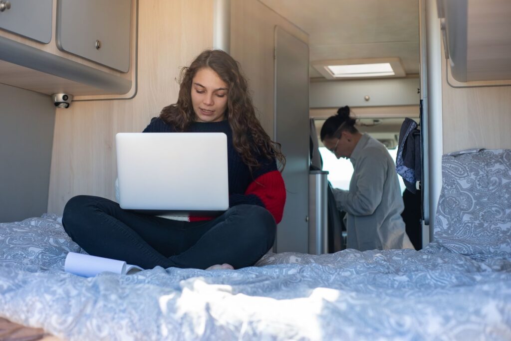 A person sitting inside a beautifully converted van, surrounded by medical supplies and a laptop displaying a telehealth appointment